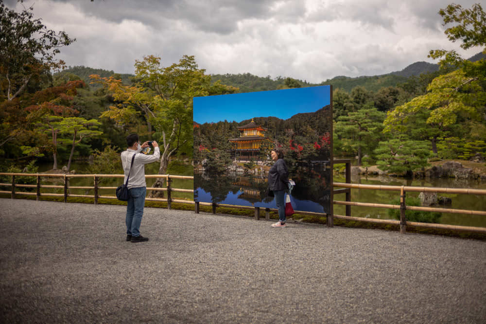 snapping a tourist photo in front of a sign in front of the shrouded golden pavilion