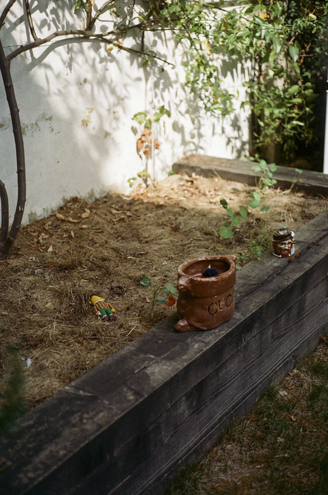 Raised garden bed with a ceramic Gucci-bag pot and small figurines